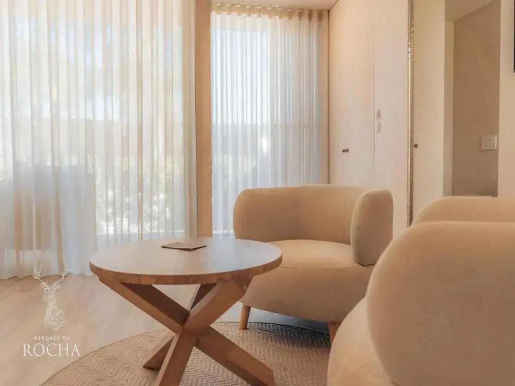 Sitzbereich im Hotelzimmer mit runden Sesseln, Holztisch und bodentiefem Fenster.