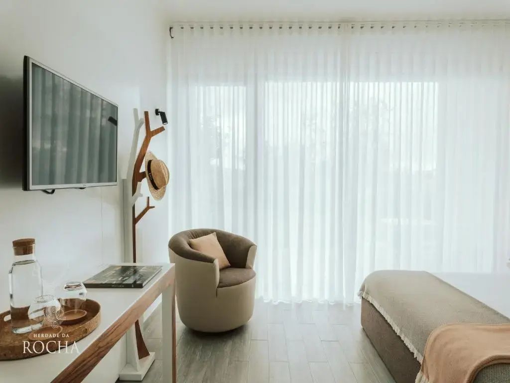 Sitzecke im Hotelzimmer mit Sessel, Fernseher und bodentiefen Fenstern.