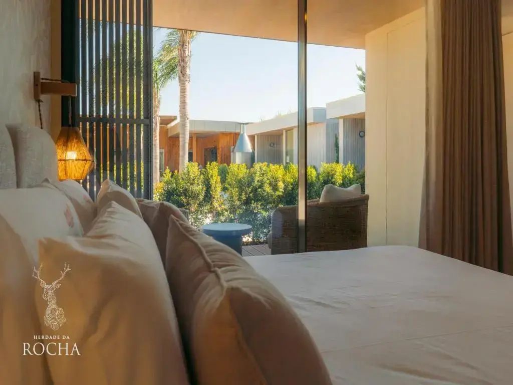 Blick vom Bett durch die große Glas-Schiebetür auf die überdachte Terrasse und den Garten.
