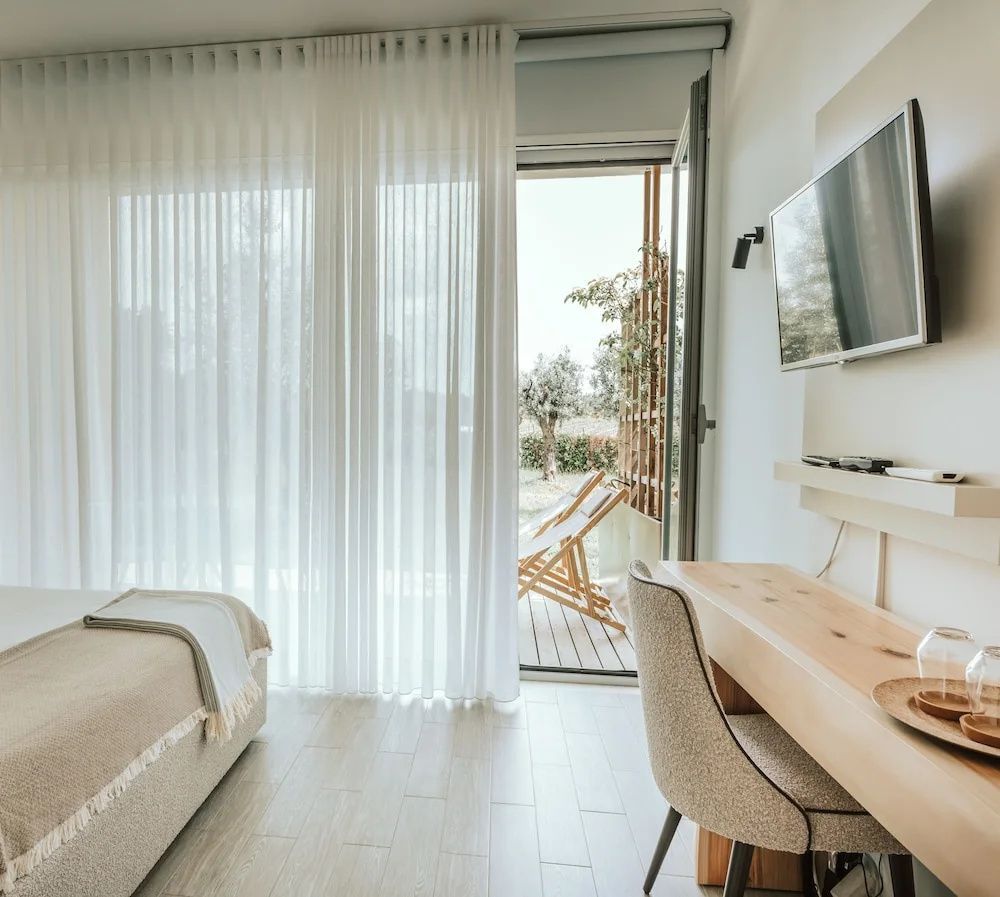 Helles Hotelzimmer mit Holzschreibtisch, Fernseher und Zugang zur Terrasse.
