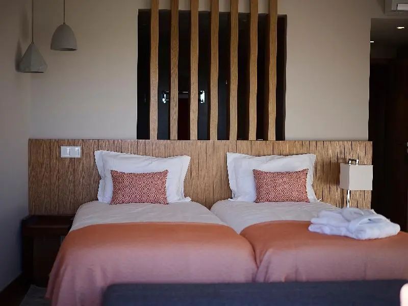 Zwei zusammenstehende Einzelbetten mit rosa Tagesdecken und Holzverkleidung an der Wand.