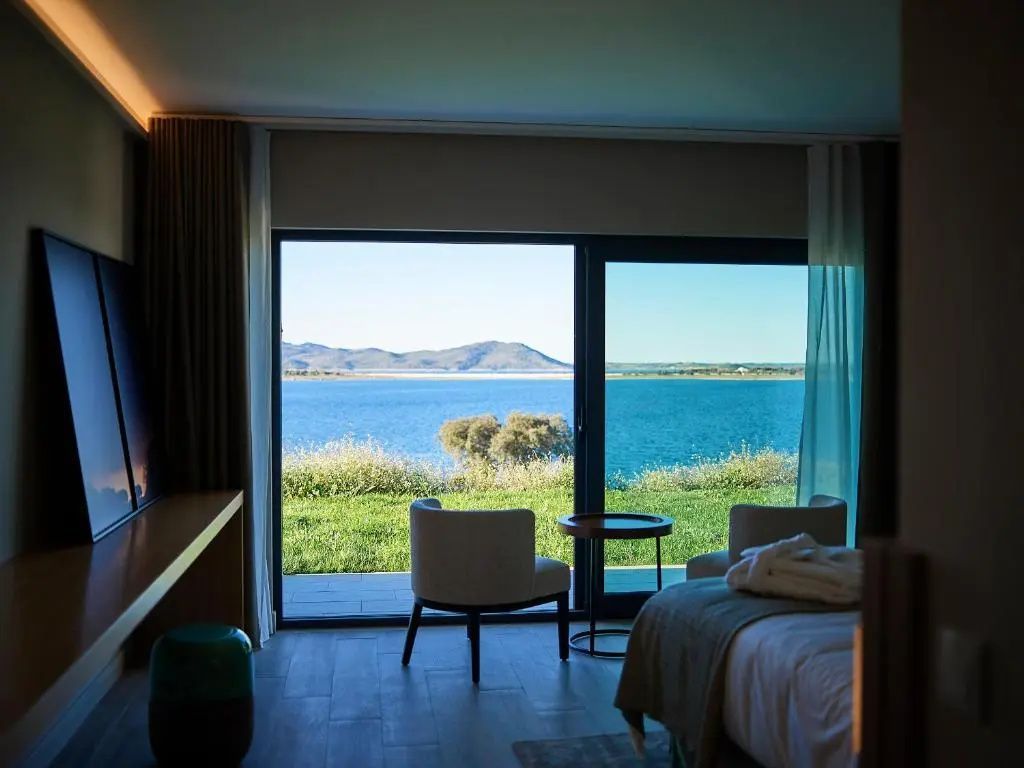 Helles Hotelzimmer mit Sitzbereich und direktem Ausblick auf die Seenlandschaft.
