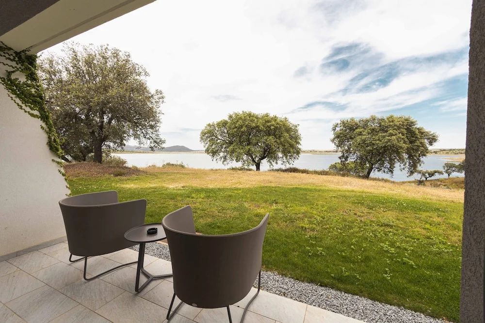 Sitzbereich auf einer Terrasse mit freiem Blick auf eine Wiese, Bäume und einen See.