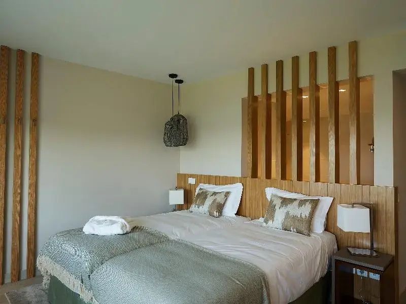 Hotelzimmer mit zwei Betten, grünen Decken, Kissen und hölzerner Wanddekoration.
