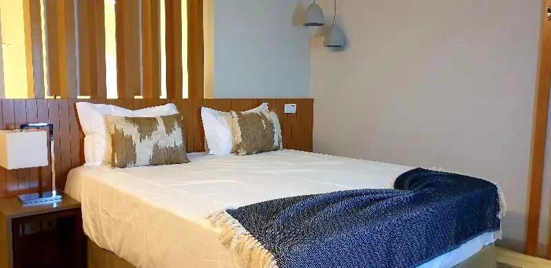 Doppelbett mit weißen Kissen, strukturierter blauer Tagesdecke und zwei hängenden Lampen.