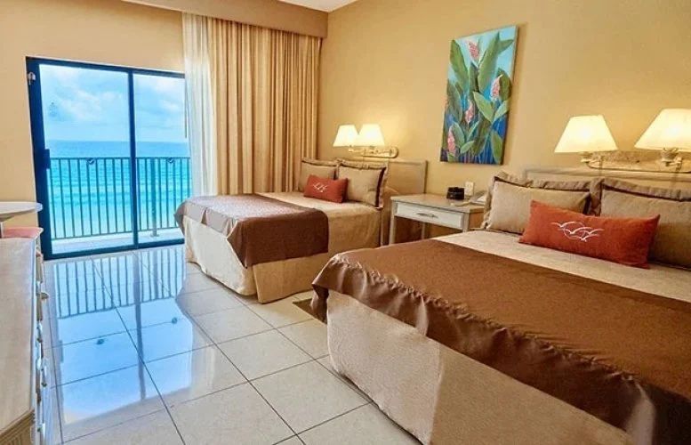 Hotelzimmer mit zwei Doppelbetten, Fliesenboden und Balkonzugang mit Meerblick.