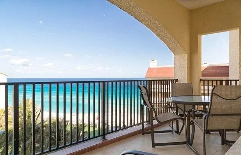Balkon mit Sitzgelegenheiten und Geländer sowie Blick auf den blauen Ozean und den Sandstrand.