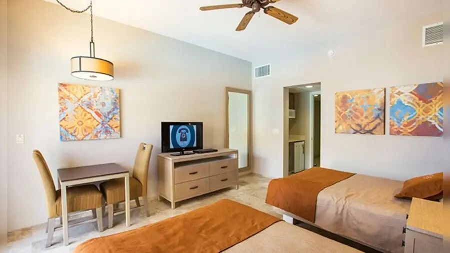 Hotelzimmer mit Flachbild-TV auf Kommode, Esstisch mit Stühlen und Wandbildern.