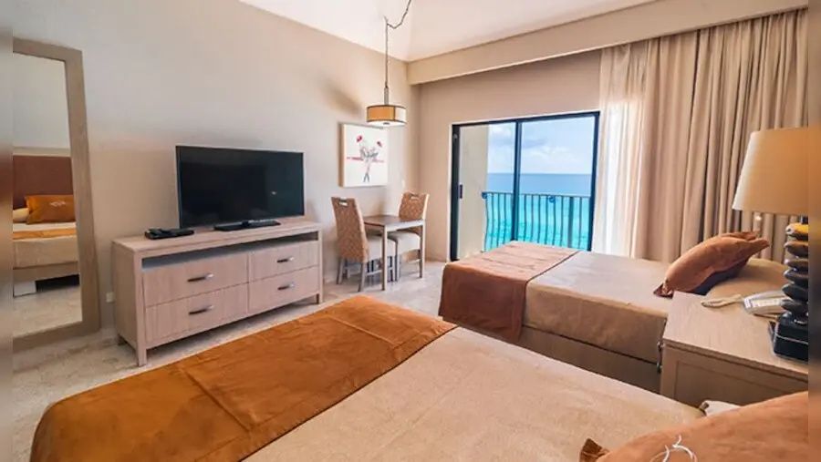 Hotelzimmer mit zwei Betten, einer Kommode mit Fernseher und Meerblick vom Balkon.