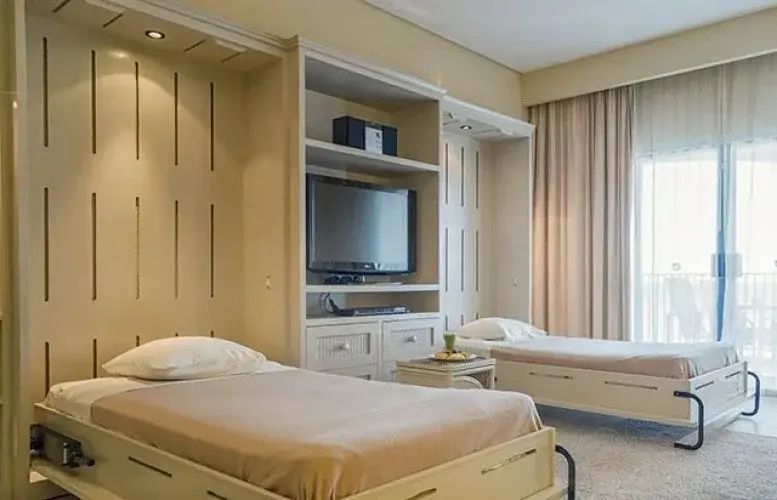 Einrichtung eines Hotelzimmers mit zwei Einzelbetten und integriertem Fernseher.