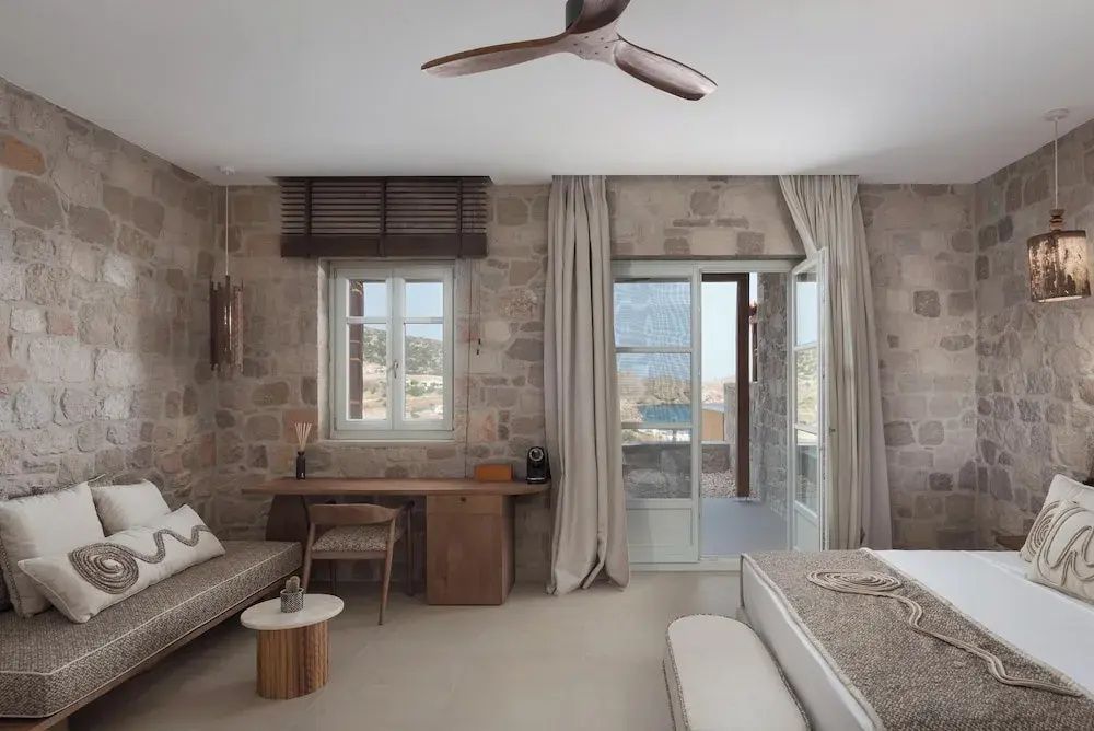 Schlafzimmer mit Steinwand, Holzschreibtisch, Deckenventilator und Tür zur Terrasse.
