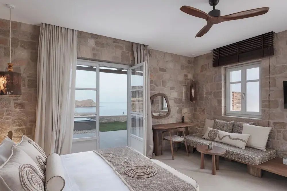 Blick durch das Schlafzimmer mit Steinwand auf die Terrasse und das Meer dahinter.