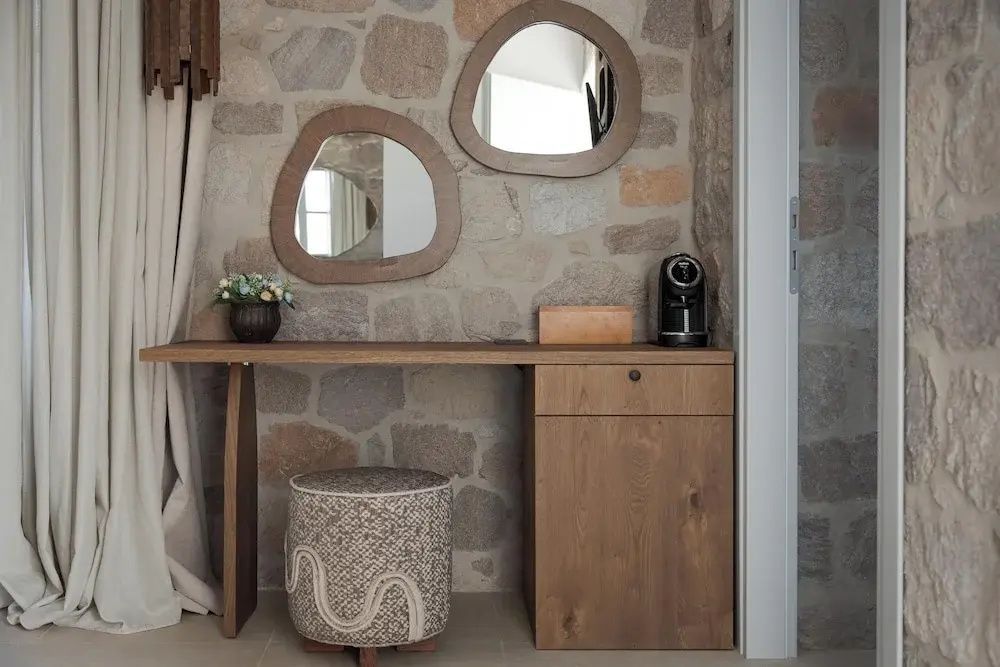 Schreibtisch aus Holz an einer Natursteinwand mit zwei organisch geformten Spiegeln.