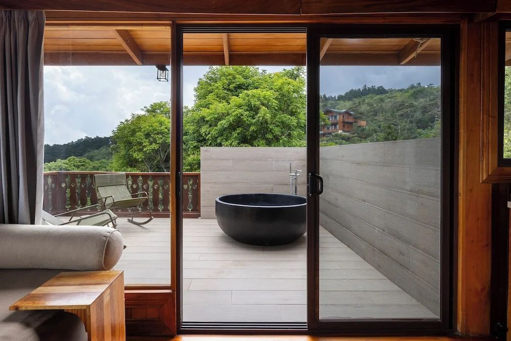 Blick durch eine Glasschiebetür auf eine Terrasse mit schwarzer Badewanne im Freien.