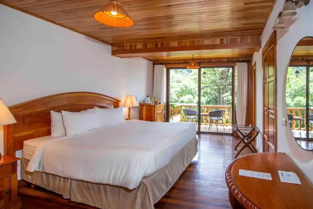 Hotelzimmer mit einem großen Doppelbett, Holzdecke und einer Glastür zum Balkon.