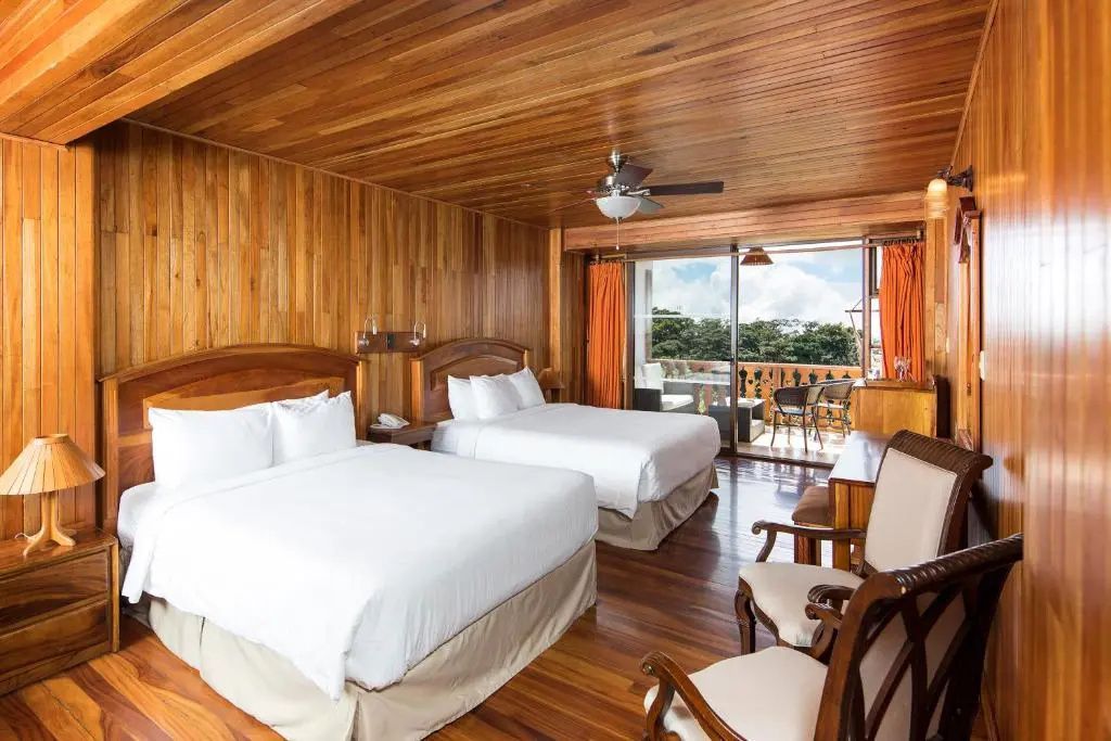 Hotelzimmer mit zwei Doppelbetten, Holzverkleidung und Balkonzugang.