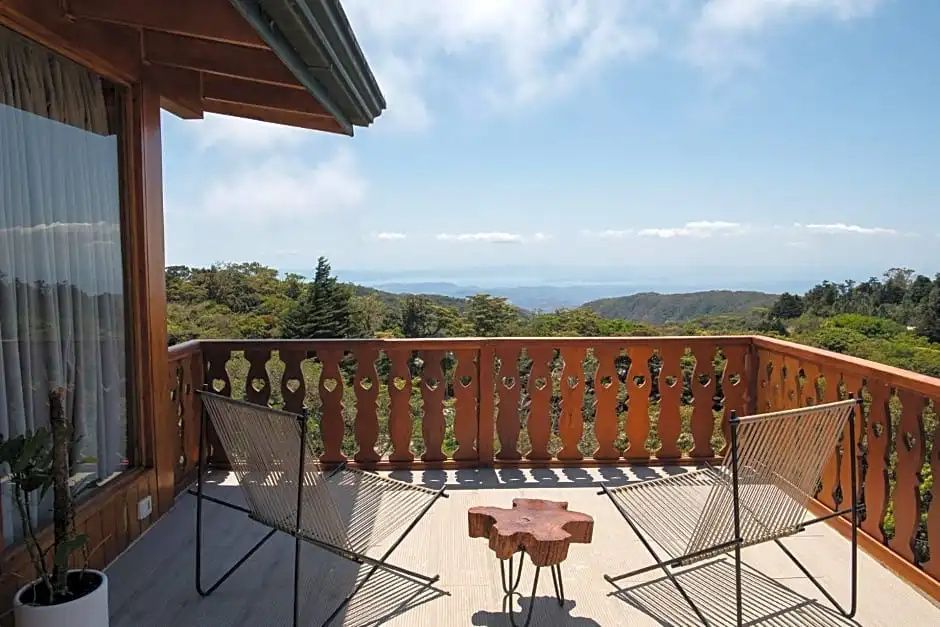 Holzbalkon mit zwei Stühlen und Weitblick über grüne Hügel bis zum Meer.