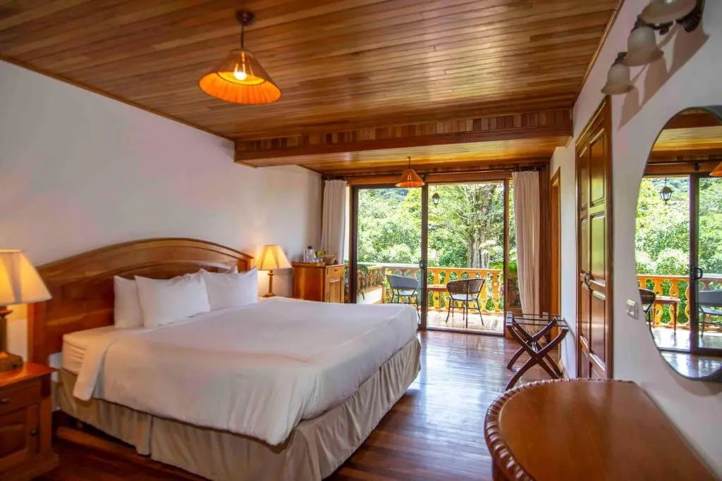 Geräumiges Hotelzimmer mit großem Doppelbett, Holzelementen und Balkon im Grünen.