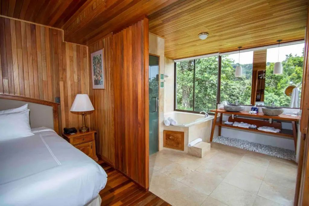 Suitenbereich mit Holzwand und integriertem Bad mit Whirlpoolwanne am Fenster.