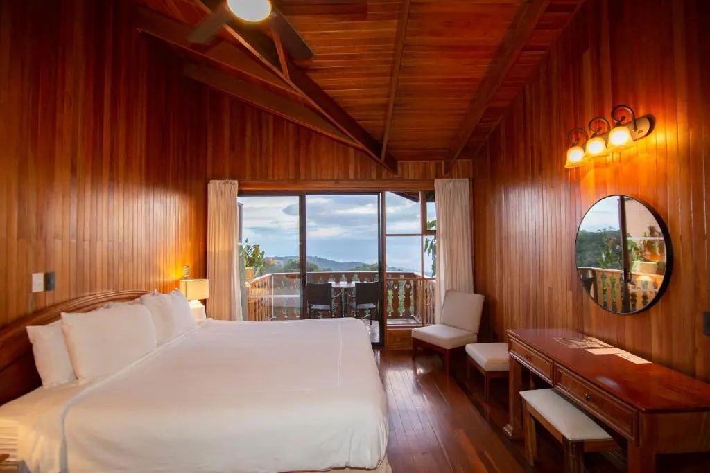 Hotelzimmer mit Holzdecke, großem Bett und Glasschiebetür zum Balkon.