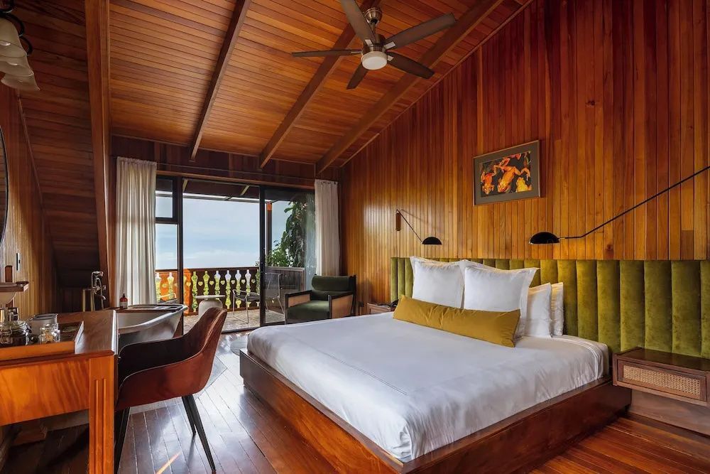 Geräumiges Zimmer mit Holzdecke, Doppelbett, grünem Kopfteil und Balkonaussicht.