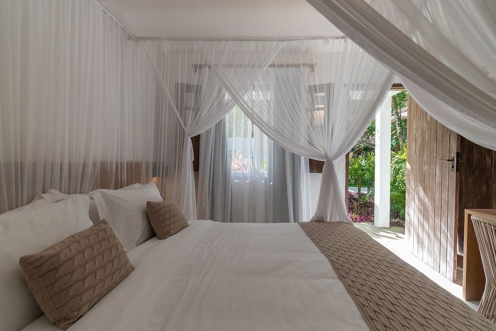 Himmelbett mit weißem Moskitonetz und Zugang zur Terrasse im Hotelzimmer