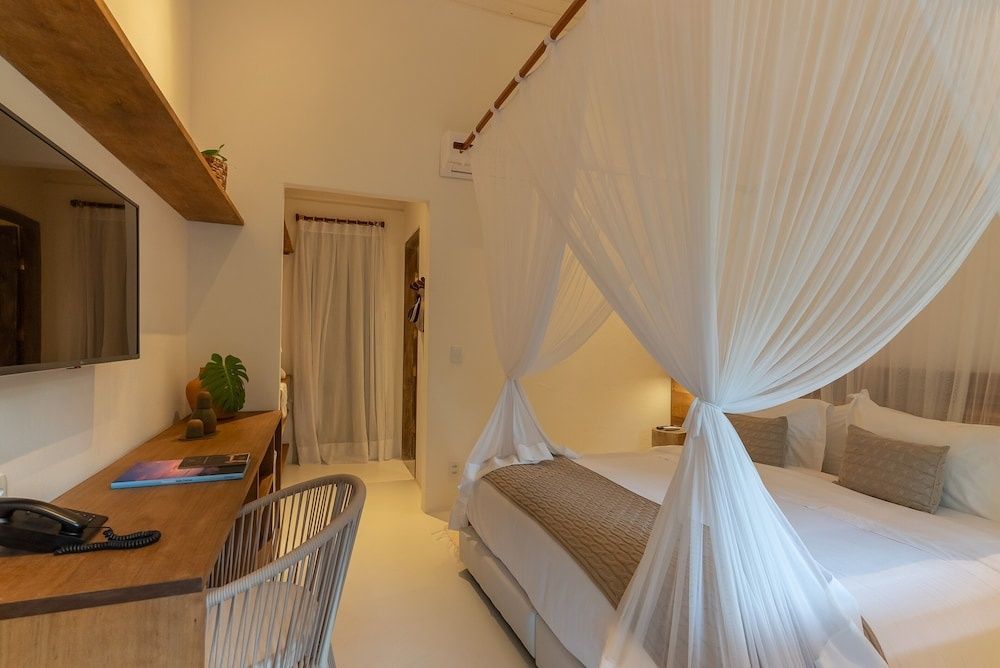Helles Hotelzimmer mit Doppelbett, weißem Fliegengitter und Holzschreibtisch mit Stuhl.