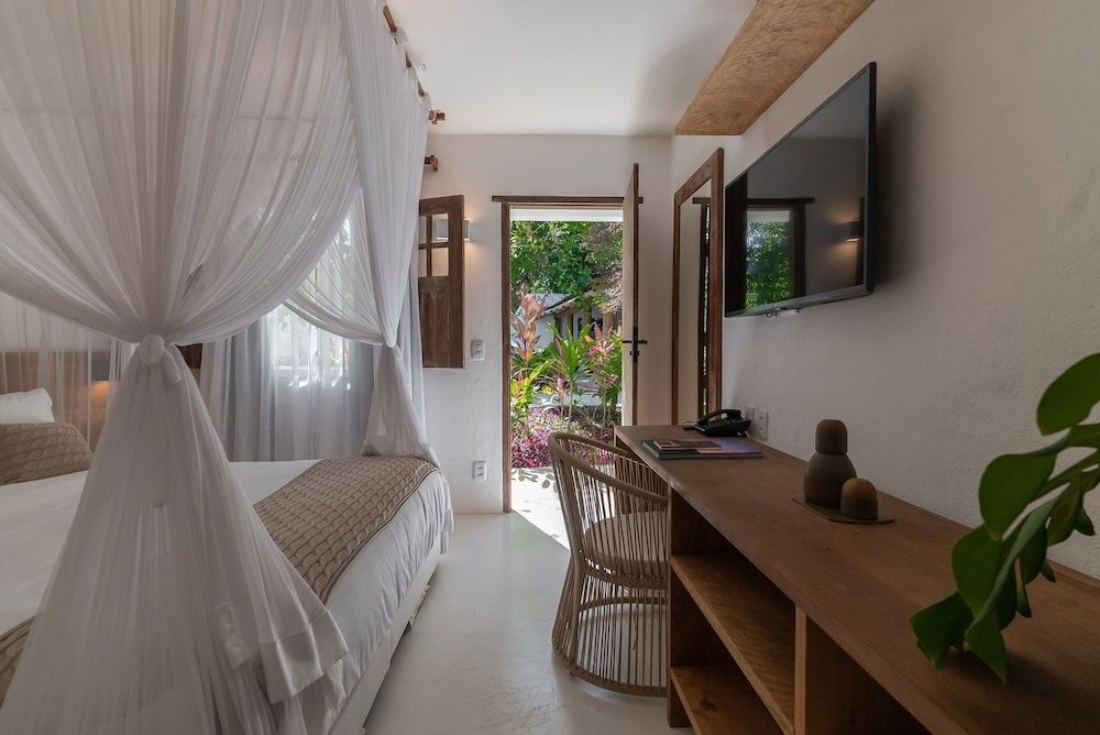 Blick durch das Schlafzimmer mit Bett und Wandfernseher auf die geöffnete Terrassentür.