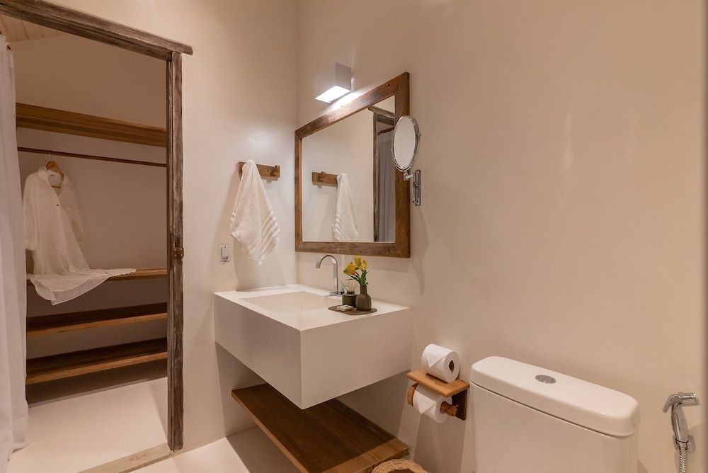 Badezimmer mit weißem Waschbecken auf Holzablage, Spiegel und Toilette.