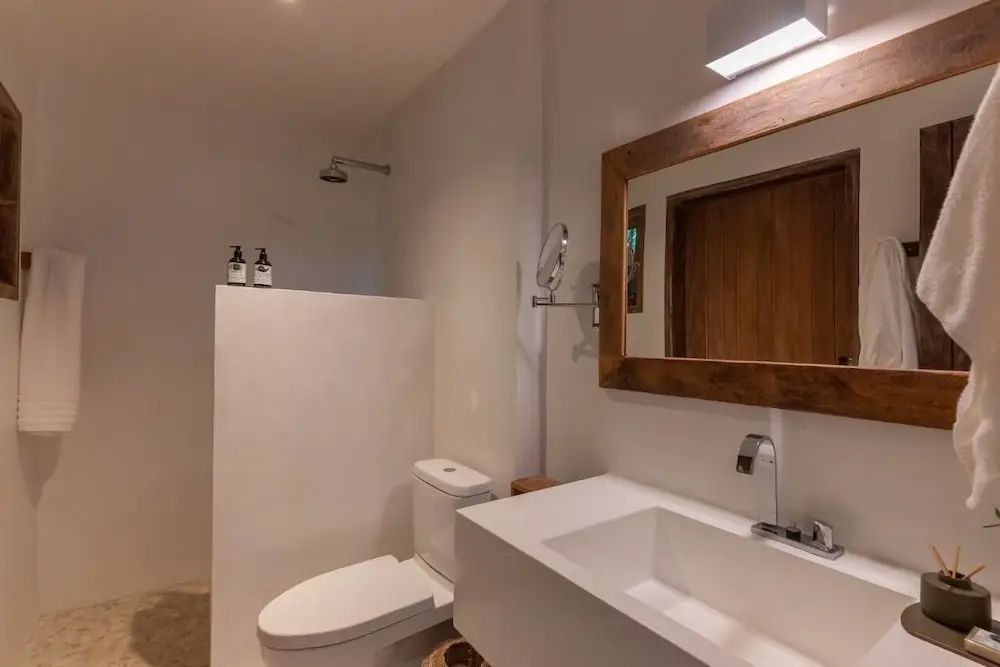 Modernes Badezimmer mit weißem Waschtisch, Spiegel mit Holzrahmen und einer Dusche.