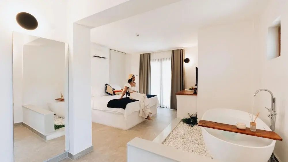 Helles Hotelzimmer mit Doppelbett, beigefarbenen Vorhängen und einer Badewanne im Raum.