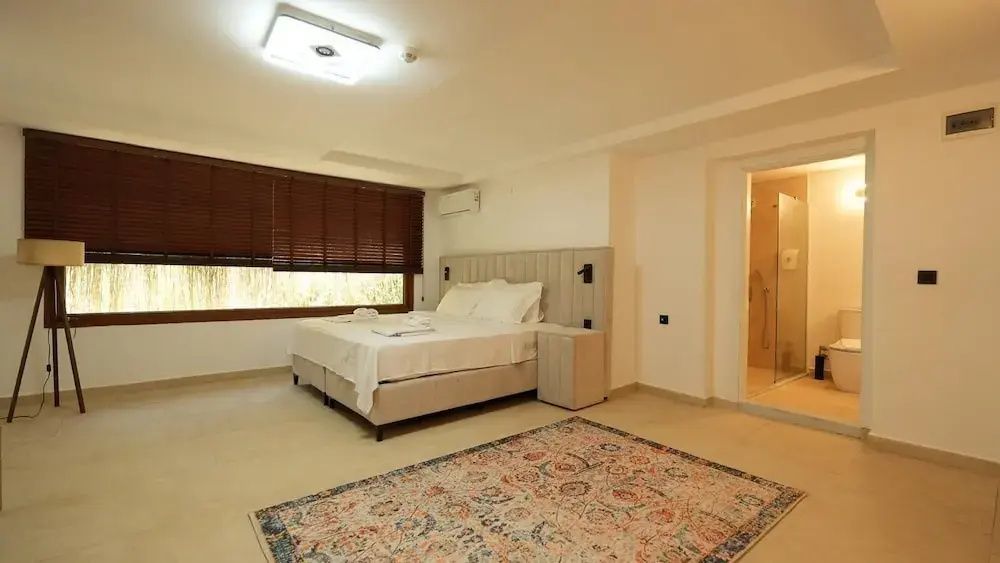 Geräumiges Hotelzimmer mit großem Doppelbett, Teppich und Blick auf das angrenzende Bad.