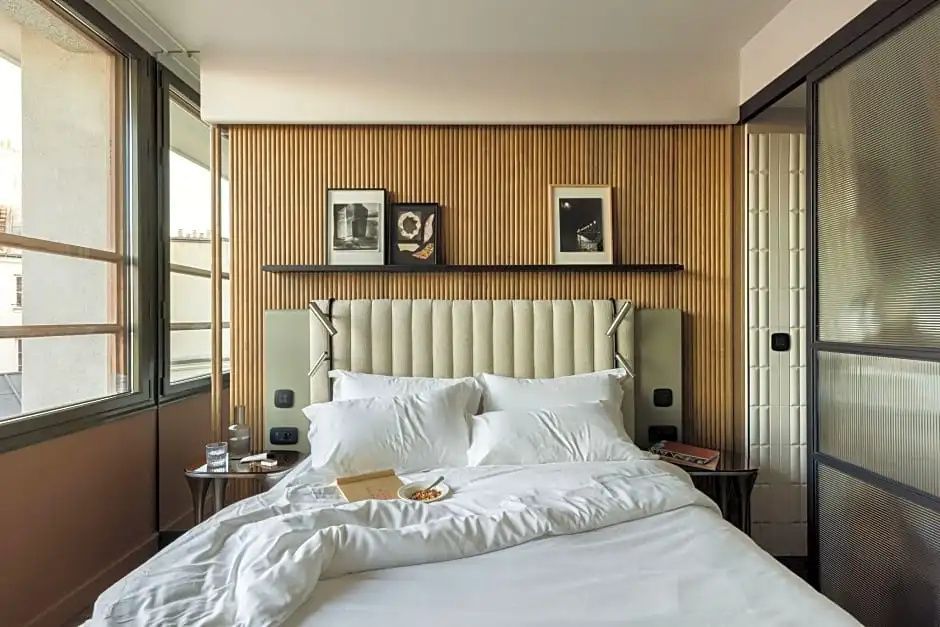 Doppelbett mit weißer Bettwäsche vor einer Wand mit Holzlamellen und kleinen Bildern.
