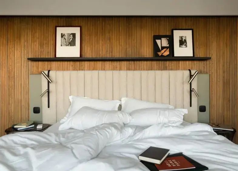 Bett mit weißer Bettwäsche vor einer Holzlamellenwand mit gerahmten Bildern.