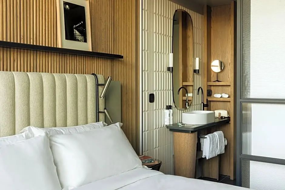 Waschbereich im Hotelzimmer mit weißem Aufsatzwaschbecken, hohem Spiegel und Handtüchern.