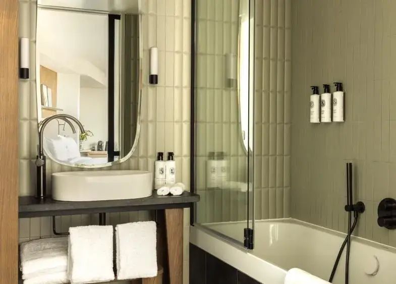 Badezimmer mit weißem Waschtisch, ovalem Spiegel, Handtüchern und Badewanne.