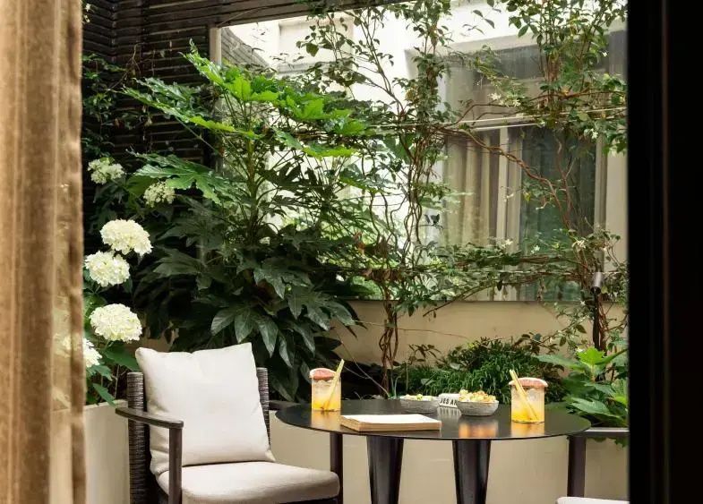 Kleine Terrasse mit dunklem Tisch, Stuhl mit Kissen und üppigen grünen Pflanzen.