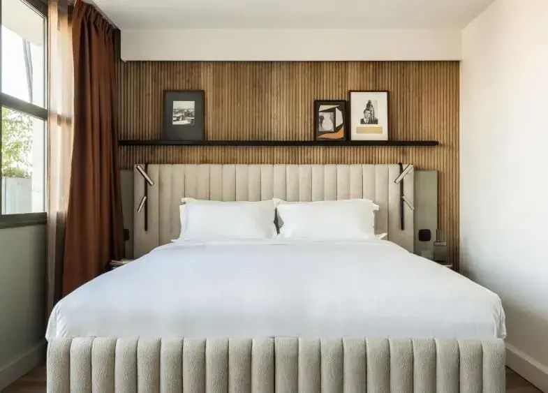 Doppelbett mit hellem Polsterkopfteil vor einer dekorativen Holzvertäfelung.