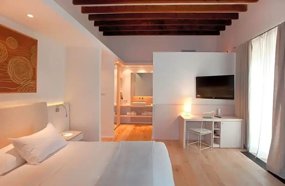 Helles Hotelzimmer mit Holzbalkendecke, Doppelbett und Schreibtisch.