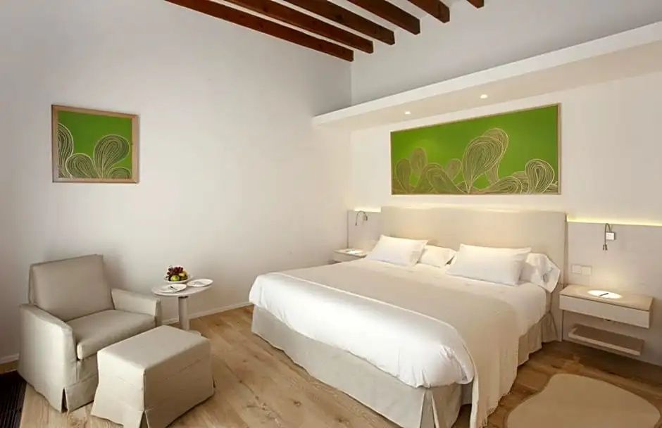 Helles Hotelzimmer mit Doppelbett, grünem Bild und Sitzbereich auf Holzboden