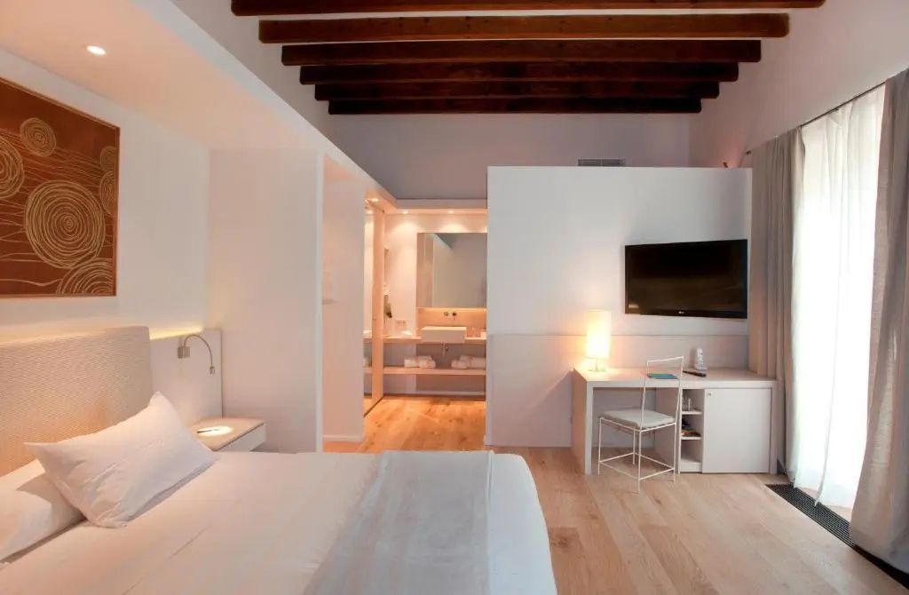 Helles Hotelzimmer mit Holzbalkendecke, Doppelbett, Schreibtisch und Wandfernseher.