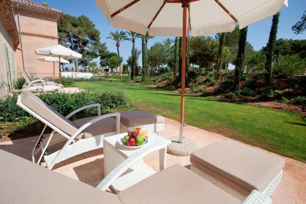 Terrasse mit Sonnenliegen, Sonnenschirm und Blick auf den grünen Garten des Hotels.