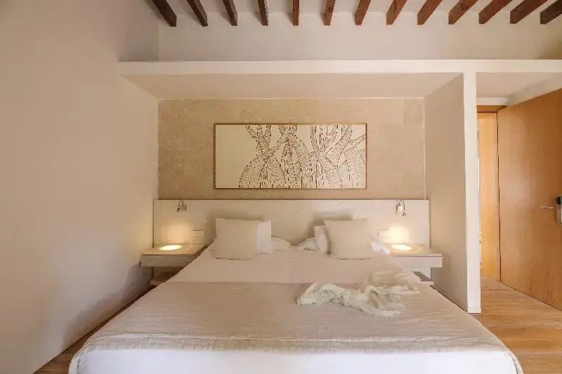 Doppelbett mit Kissen und Decke unter einer Holzbalkendecke mit Bild an der Wand