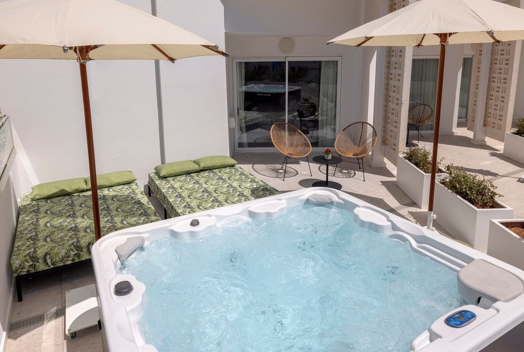 Sonnige Terrasse mit Whirlpool, bequemen Sitzgelegenheiten und zwei Sonnenschirmen.