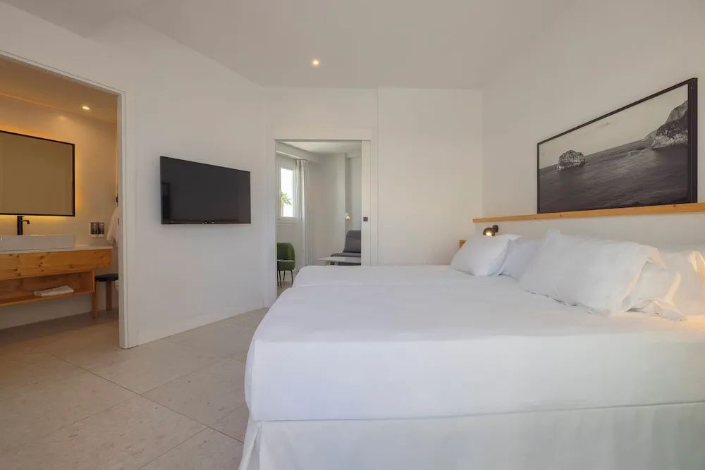 Helles Hotelzimmer mit weiß bezogenem Doppelbett und Fernseher an der Wand.