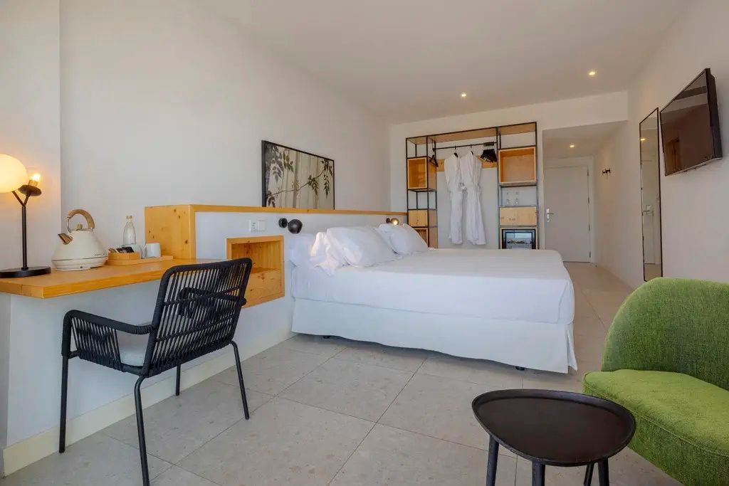 Helles Hotelzimmer mit Doppelbett, Schreibtisch und offenem Kleiderschrank aus Holz.