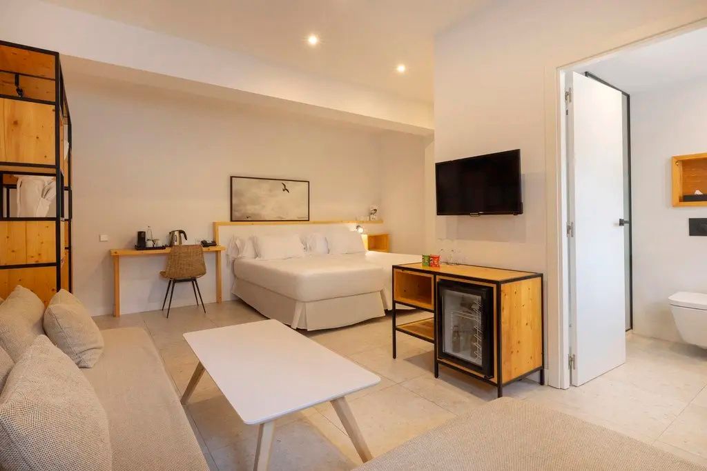 Helles Hotelzimmer mit Doppelbett, Flachbild-TV und weissem Couchtisch im Sitzbereich.