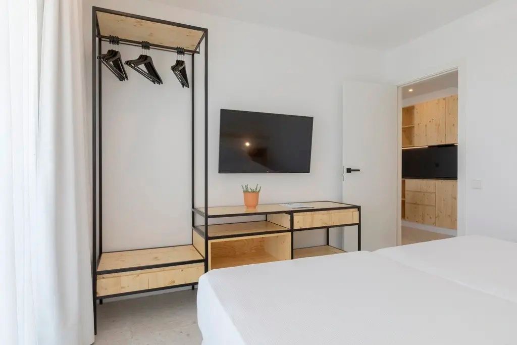 Offenes Garderobenregal aus Holz und schwarzem Metall neben einem Wandfernseher im Zimmer.