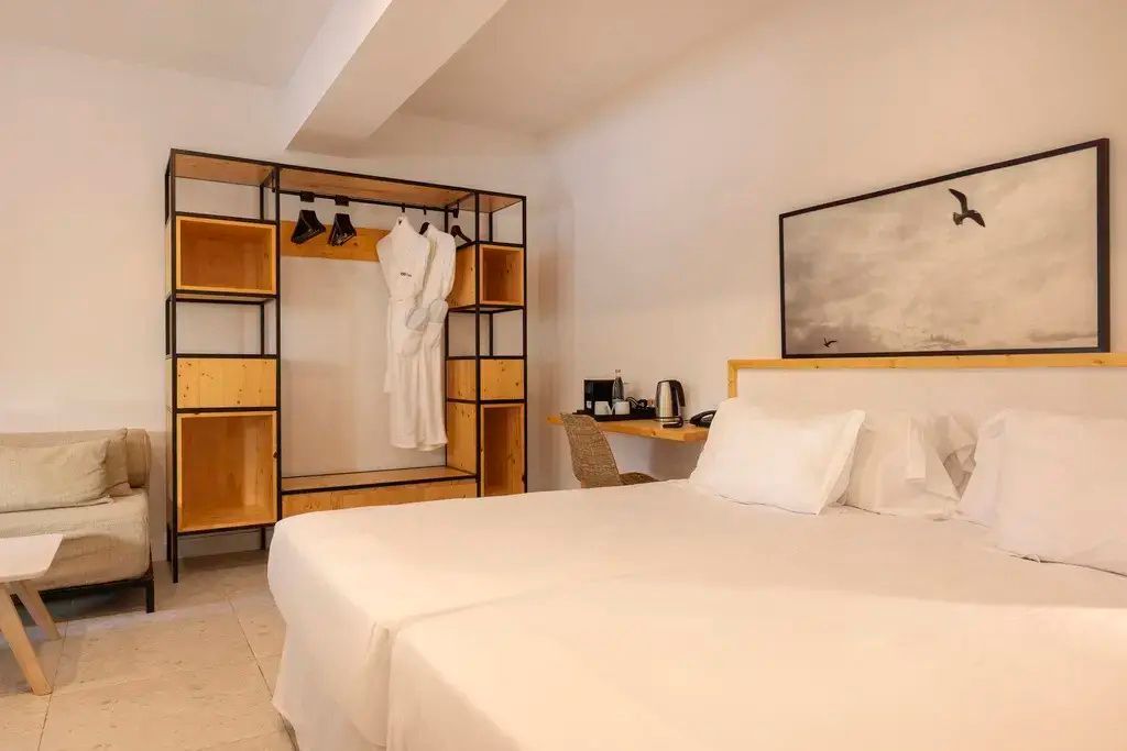 Hotelzimmer mit Doppelbett, offenem Kleiderschrank aus Holz und Schreibtischbereich.