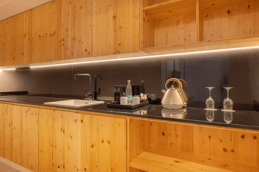 Küchenzeile mit Holzelementen, dunkler Arbeitsplatte, Wasserkocher und Kaffeemaschine.